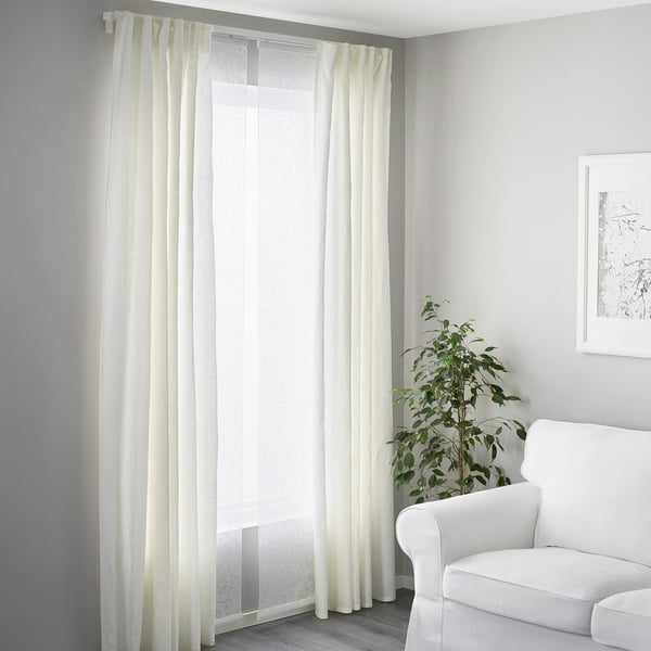 Minimalist living room with white decor, VIDGA curtain system filters light and sound, armchair, plant, wall art.