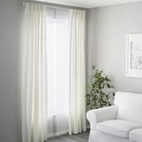 Minimalist living room with white decor, VIDGA curtain system filters light and sound, armchair, plant, wall art.