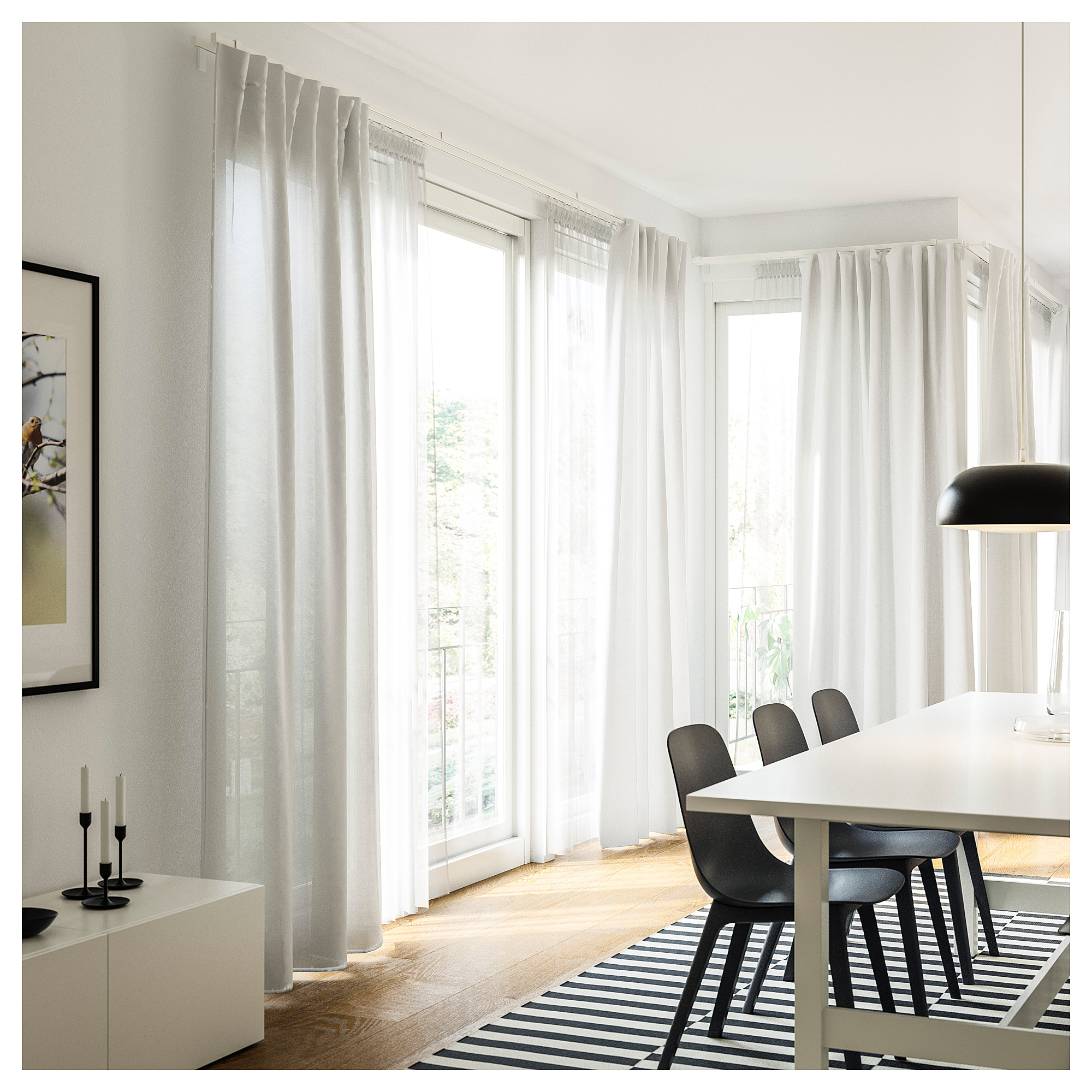 Minimalist dining room with large windows, white table, black chairs, striped rug, and black candlesticks.