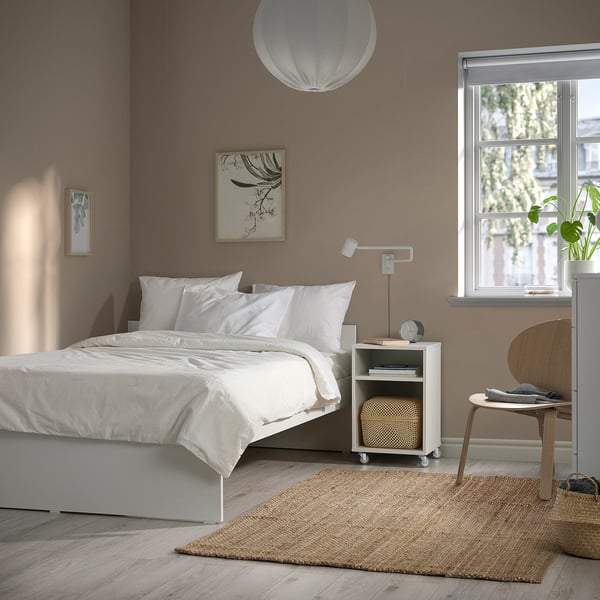 Bedroom with modern, white VIHALS bed centered against brown wall, complemented by simple wooden side table, and cascading lamp.