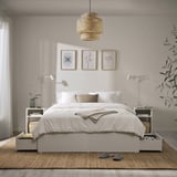 Minimalist bedroom with white VIHALS bed, built-in storage, jute rug, pendant light, botanical prints, and bed lamps.