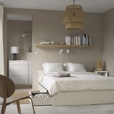 Modern bedroom with white bed, storage, wooden chair, dresser, and shelves.