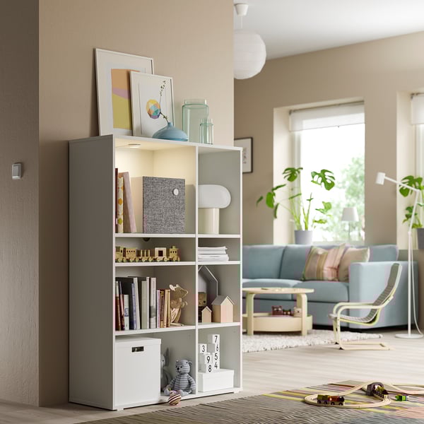 Cozy living room with a VIHALS white shelving unit, holding books, toys, and decor. Light blue sofa, wooden coffee table, and plants are visible.