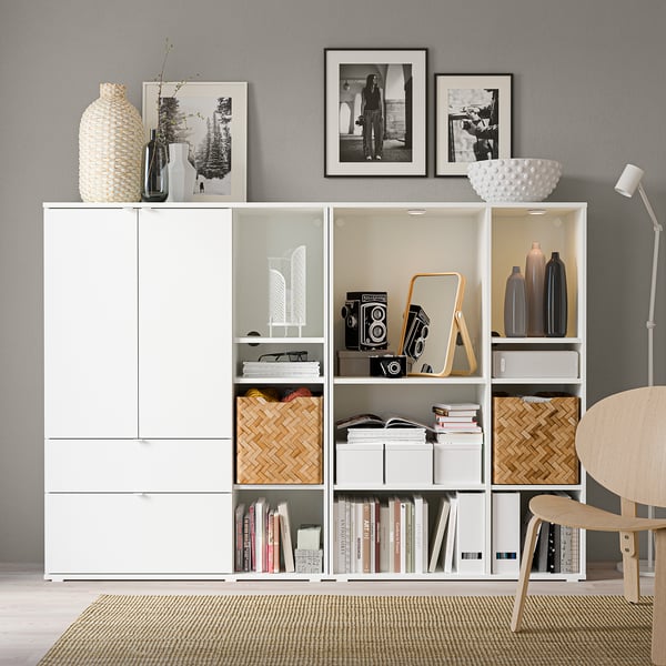 Modern room with white storage units, vintage cameras, books, and vases. Black & white photos on wall, chair, and lamp.