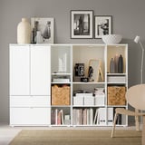 Modern room with white storage units, vintage cameras, books, and vases. Black & white photos on wall, chair, and lamp.