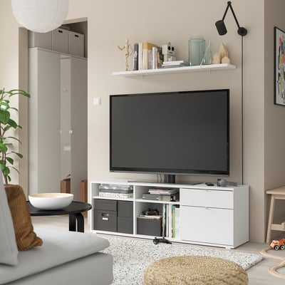 White tv stand with shelves. Flat screen tv, books, and home decor. White couch and rug.