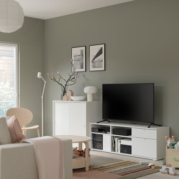 Modern living room with white tv stand, beige chair, colorful rug, and green walls.