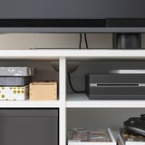 Modern white storage unit with gray shelves holds boxes, electronics, and games. Clean design, cable management, and wedge-dowel assembly.