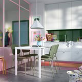 Modern kitchen with VIHALS white table and green chairs, pink accents, hanging lamp, colorful rug, and various utensils.
