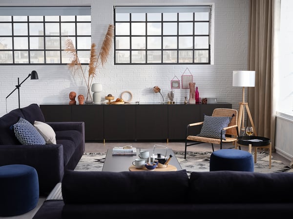 Modern living room: dark grey VIMLE sofa, patterned rug, coffee table with cups, black console, wicker chair, large windows.
