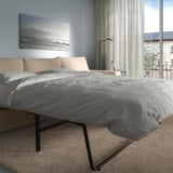 Modern bedroom with VIMLE sofa-bed, city view, & beach art.