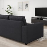 A modern black VIMLE sofa with a chaise longue, positioned in a living room with wooden floors. It is accompanied by a flat-screen tv and a rug.