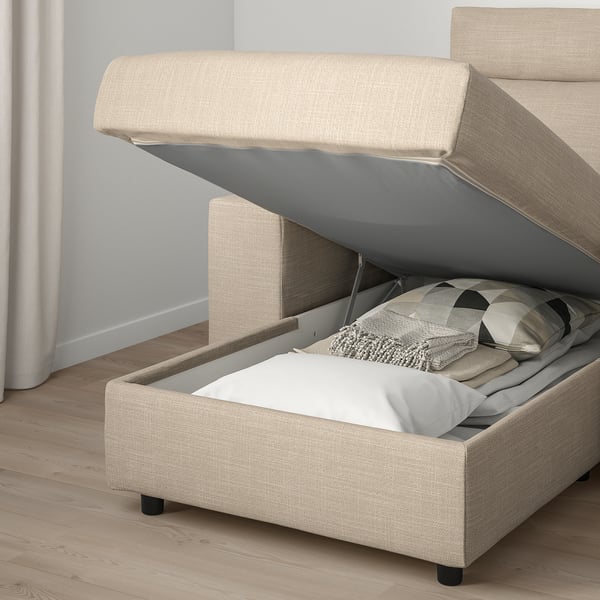 Bed or sofa with storage compartment open, showing pillows and blanket inside. Lid stays open for easy access.