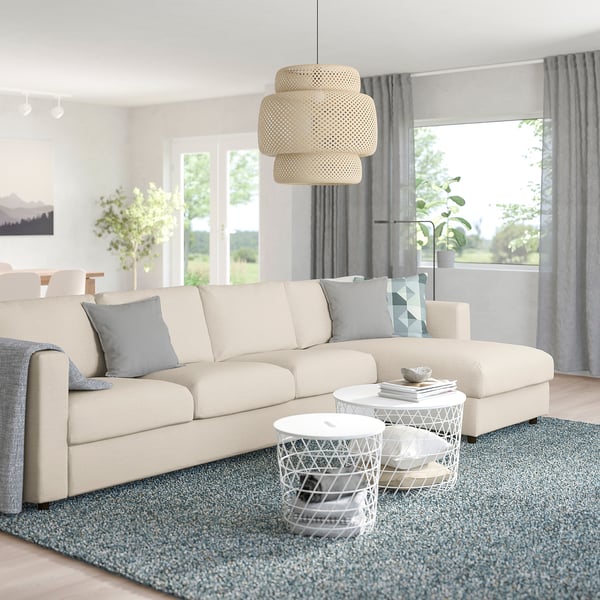 Modern living room with cream l-shape sofa, small coffee tables, pendant lamp, gray rug and curtains, natural light.