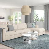 Modern living room with cream l-shape sofa, small coffee tables, pendant lamp, gray rug and curtains, natural light.