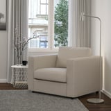 Its a VIMLE beige sofa chair in a minimalist room, adjacent to a tall lamp and small table holding a vase and mug.