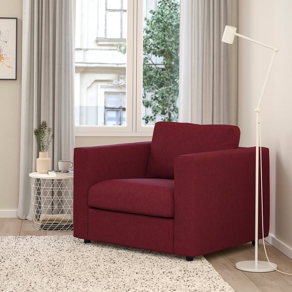 Red armchair by window with lamp, decor, rug.
