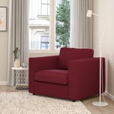 Red armchair by window with lamp, decor, rug.