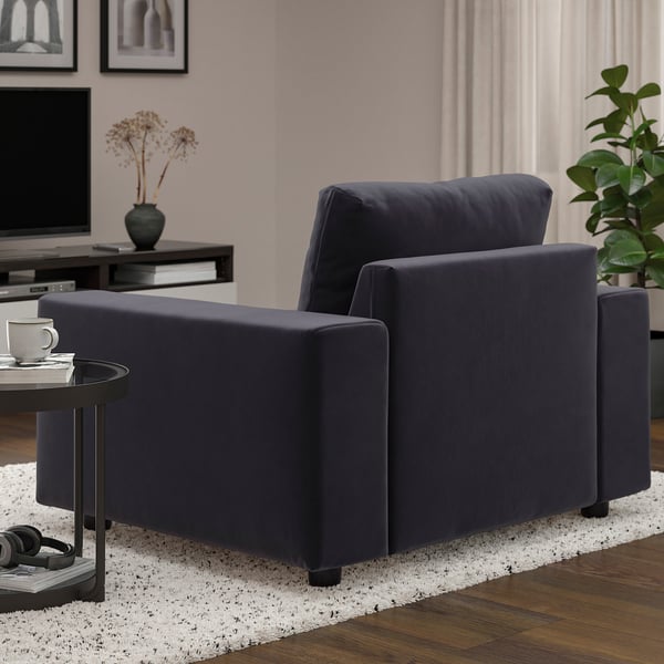Dark blue modern sofa in living room with wooden floor, white rug, and side table with coffee cup.