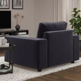 Dark blue modern sofa in living room with wooden floor, white rug, and side table with coffee cup.