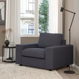 Modern gray armchair in living room. Next to side table with vase and lamp. Medium size compared to surroundings.