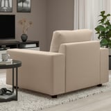 A light beige upholstered armchair in a living room with a black side table holding a mug and headphones.