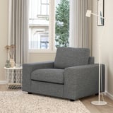 Gray VIMLE accent chair, lamp, side table with vases, by large window with curtains. Cozy, minimalist room with rug.
