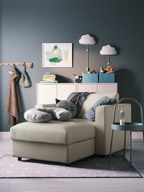 Cozy living room with VIMLE beige sofa, gray creature pillows, side table, and colorful bookcase against green wall.