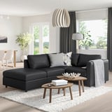 Modern living room VIMLE black leather sofa with grey cushions, wooden side tables, large window with curtains, and potted plants.