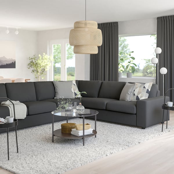 Minimalist living room with grey VIMLE sofa, glass coffee table, decor, pendant light, black curtains, floor lamp, serene outdoor view.