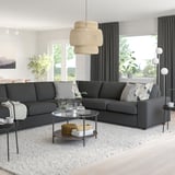 Minimalist living room with grey VIMLE sofa, glass coffee table, decor, pendant light, black curtains, floor lamp, serene outdoor view.