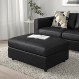Black VIMLE ottoman, upholstered in leather. Square shape, fits near matching sofa, with open book on top.
