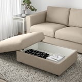 A beige VIMLE sofa with an ottoman. The ottomans seat is lifted, revealing storage space with magazines and folded fabric inside.