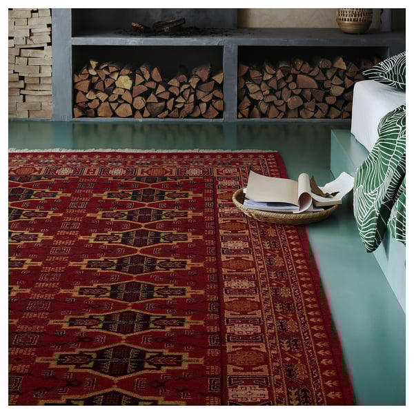 Burgundy geometric rug on teal floor, beside stacked logs and cushions.