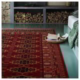 Burgundy geometric rug on teal floor, beside stacked logs and cushions.