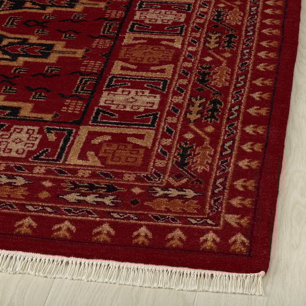 Red area rug with gold and black patterns on wooden floor.