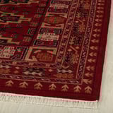 Red area rug with gold and black patterns on wooden floor.