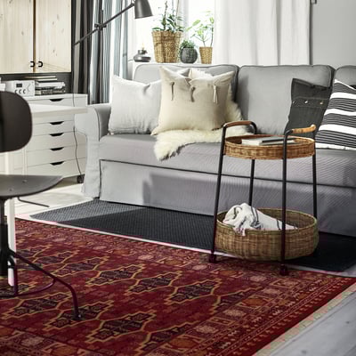 Red geometric rug, grey couch, black chair, side table with basket.