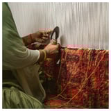 Person weaving colorful, handmade rug.