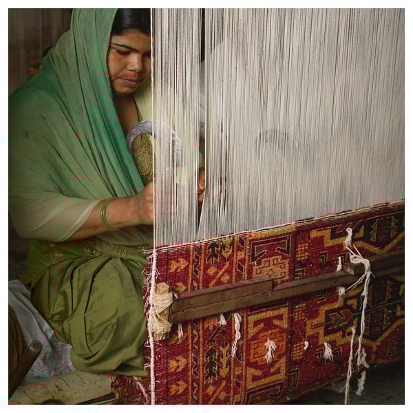 Woman weaving colorful rug. Green attire, intricate patterns.