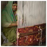 Woman weaving colorful rug. Green attire, intricate patterns.