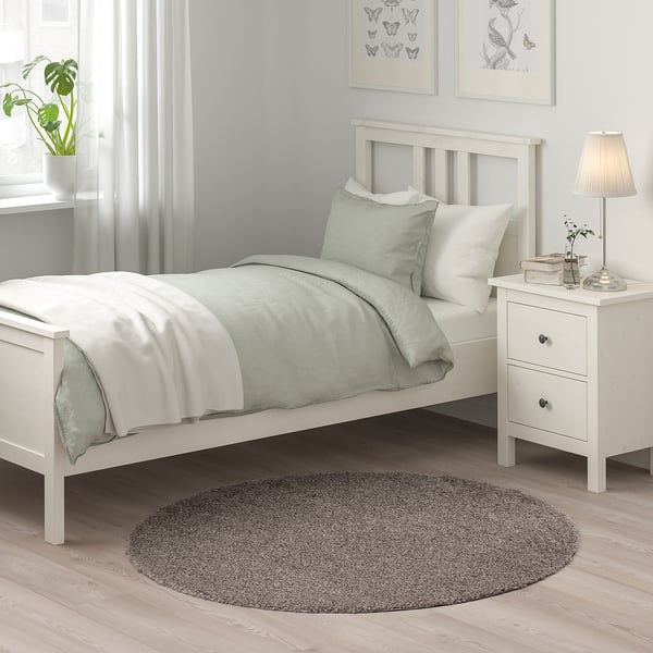 Cozy bedroom with single bed, gray rug, nightstand, and lamp.