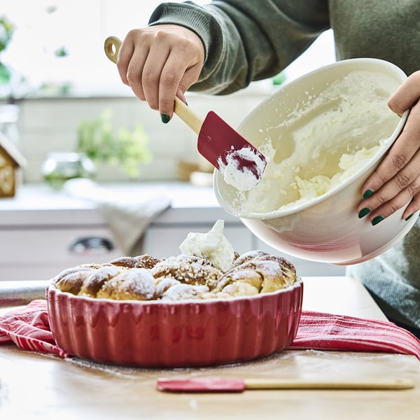 A person uses a bamboo spatula with a silicone tip to spread icing evenly. It hangs near the cooking area for easy access.