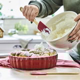 A person uses a bamboo spatula with a silicone tip to spread icing evenly. It hangs near the cooking area for easy access.