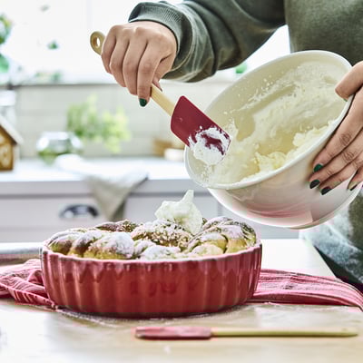 A person uses a bamboo spatula with a silicone tip to spread icing evenly. It hangs near the cooking area for easy access.