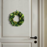 A green plant wreath hangs on a white door, adding natural decor and a welcoming touch.