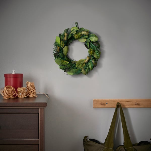 Small wreath of dried plants hangs above a drawer with a red container and woven baskets, next to a wooden coat hook with a green bag.