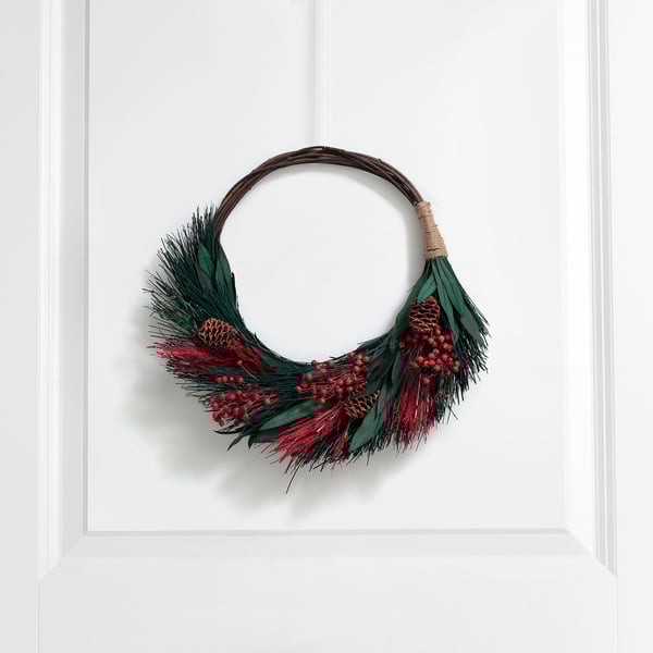 A winter wreath with greenery, red berries, and pine cones hangs on a white door, bringing a natural, welcoming charm.