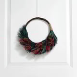 A winter wreath with greenery, red berries, and pine cones hangs on a white door, bringing a natural, welcoming charm.