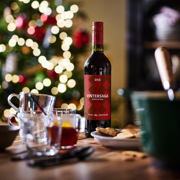 Bottle of IKEA VINTERSAGA mulled red wine beside glasses, cookies, and christmas tree lights.
